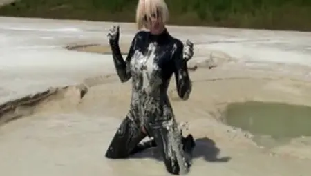 Super Hot Blond Girl In Black Latex Catsuit + High Heels And Sunglasses Bathes In The Mud - Mud Bath
